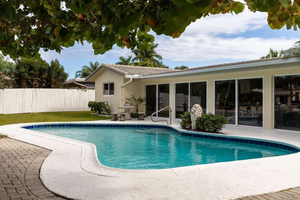 Modern backyard with pool, artificial grass, stone path, trees, and patio chairs