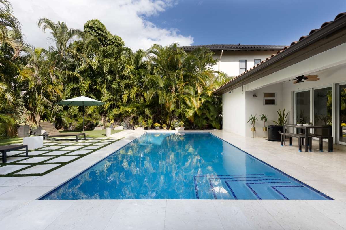 Modern backyard with pool, artificial grass, stone path, trees, and patio chairs