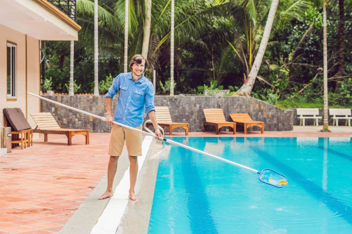 Pool cleaner in blue shirt with equipment beside a sunny swimming pool