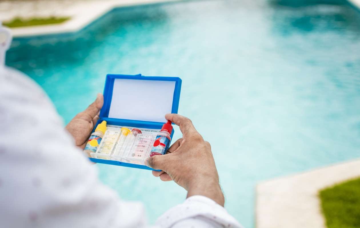 Hand holding a pool water test kit with blurred pool in background
