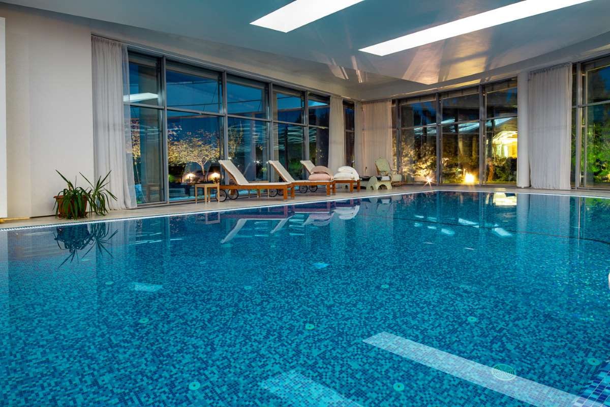 Indoor villa pool overlooking a park at dusk through wide windows