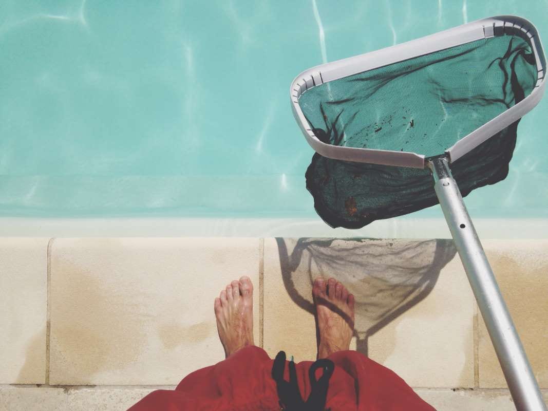 Person holding a fishing net beside a swimming pool