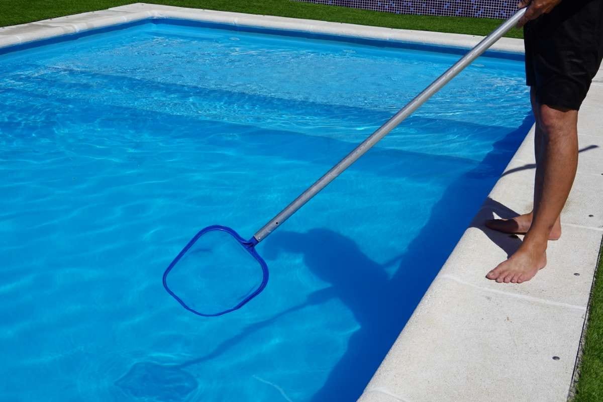 Man cleaning pool surface with a mesh skimmer