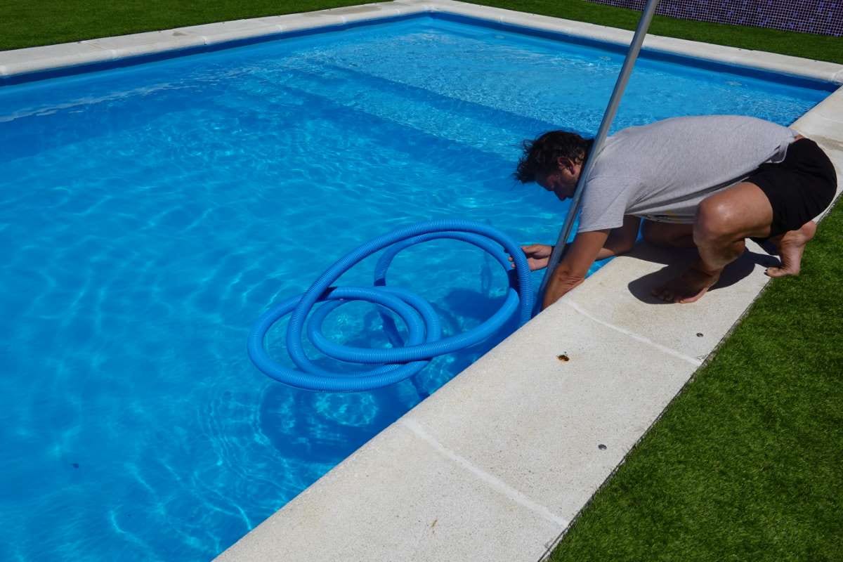 Man connecting a pool cleaner pipe beside a summer swimming pool
