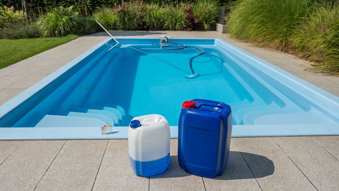 Poolside scene with chemical containers, cleaning hose, and water testing kit