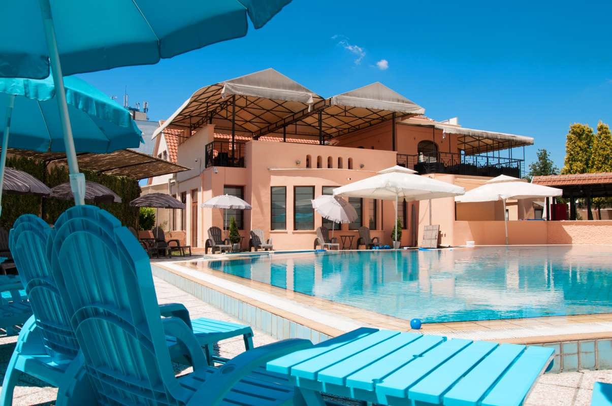 Quiet outdoor poolside seating with umbrella, tree, and building under a blue sky