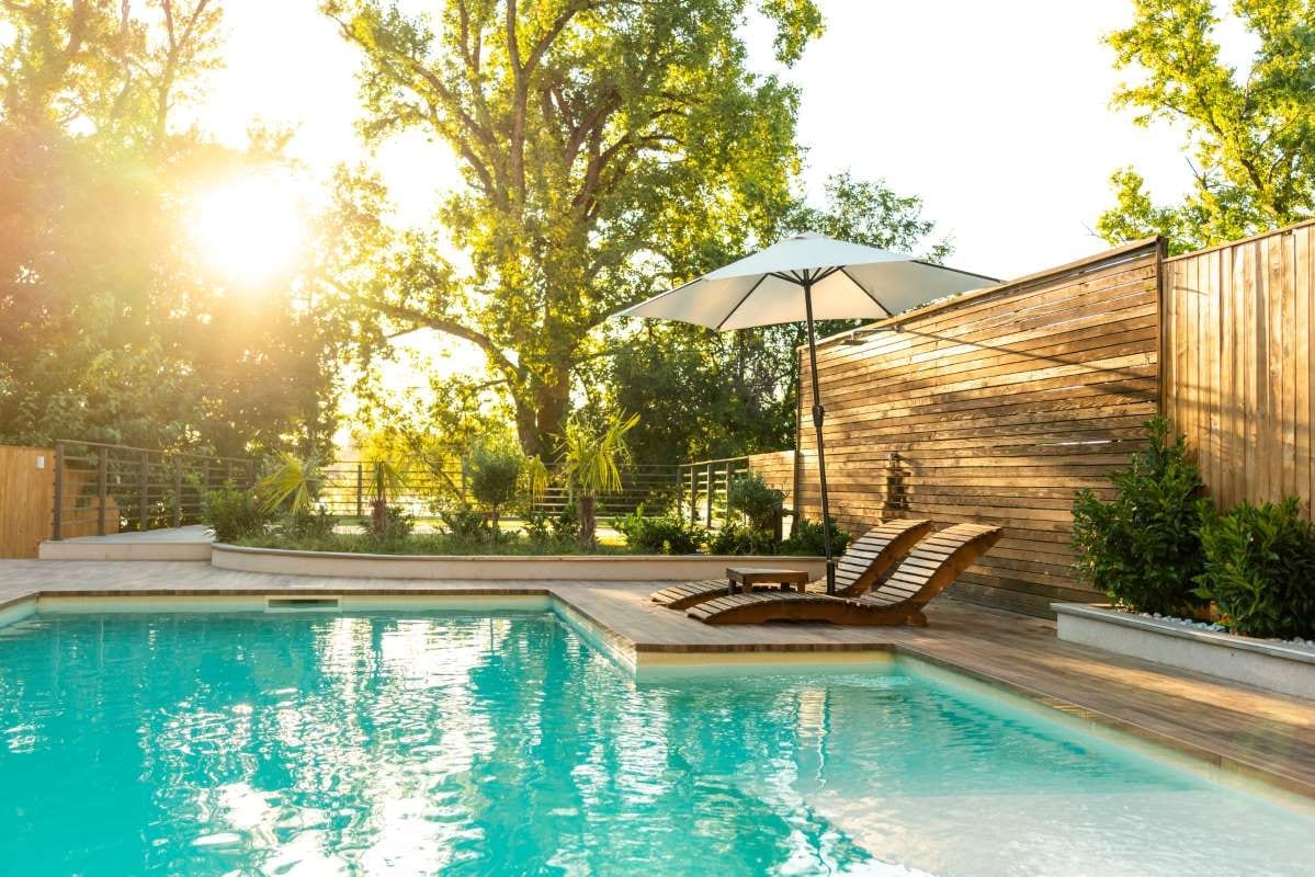 Modern private villa pool with lounge chairs, palm trees, and umbrella